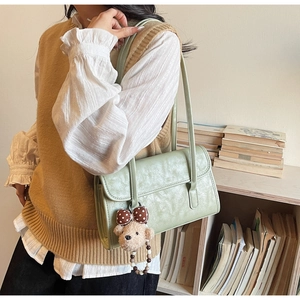 Detail of light green faux leather shoulder bag with cute teddy bear charm and retro texture