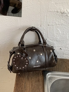 Vintage dark brown Boston bag with star studs and heart pendant on a wooden surface
