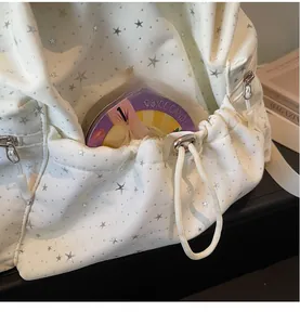 Detailed view of white fabric backpack featuring silver stars and side drawstring pocket
