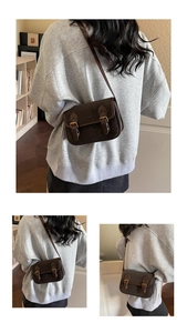 Détail d'un sac à bandoulière rétro marron foncé avec deux boucles dorées et cuir texturé