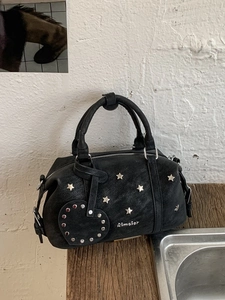 Vintage black Boston handbag with silver star studs and heart pendant on a wooden surface