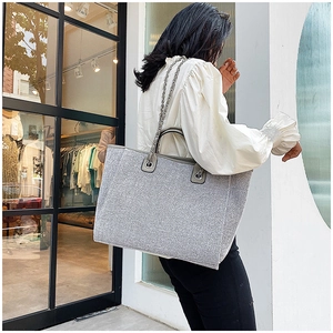 Bolso tote gris moderno de gran capacidad con cadena plateada en una toma de estilo urbano
