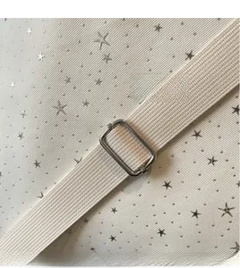 Detail of adjustable woven cream shoulder strap with silver metal buckle on star pattern bag