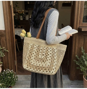 Detail of woven straw tote bag featuring crochet flower patterns and leather handles