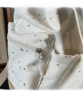 Detailed close-up of smooth metal zipper and silver star pattern on white backpack fabric