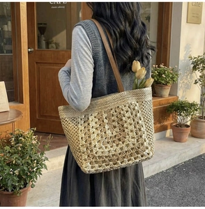 Macro detail of hand-woven straw tote bag with brown leather straps in a cafe setting