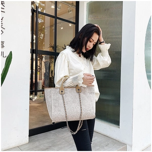 Detalle del bolso de tweed beige con asas dobles y correas de cadena metálica fina