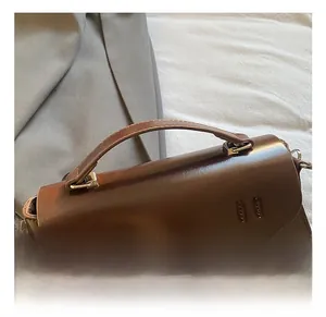 Detail shot of a dark brown leather satchel showing a curved handle and stitched flap cover