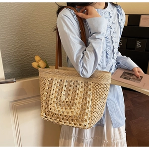 Detail showing the woven texture and brown leather strap of the straw tote bag