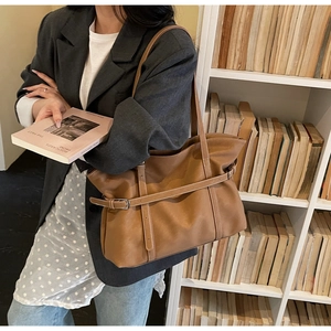 Braune Vintage-Einkaufstasche mit Zierriemen und weißen Nähten vor einem Bücherregal