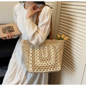 Detail of beige hollow woven straw tote bag featuring brown leather straps and spacious interior