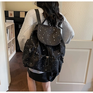 Detailed back view of a black star-patterned backpack with flap cover on a female model