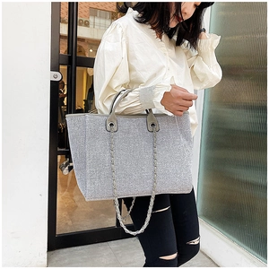 Detalle de bolso tote con lentejuelas plateadas, asas de cuero gris y cadena metálica