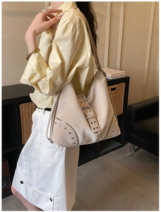 Detail view of cream shoulder bag with silver rivet buckles and vintage moto style design