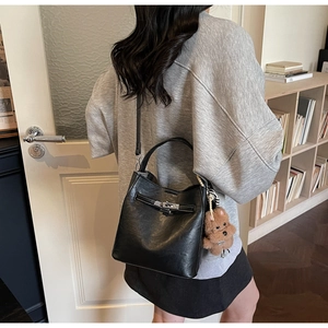 Détail d'un sac seau en cuir noir avec boucle argentée et charm d'ours en peluche