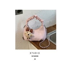 Détail d'un sac à main plissé rose avec pendentif ours en peluche sur bois verni
