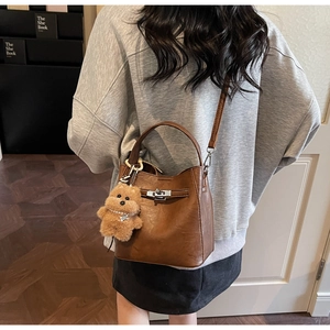 Détail d'un sac seau en cuir marron avec fermoir rotatif en métal et breloque ours en peluche