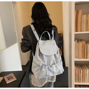 Light blue backpack with star patterns and drawstring closure worn by a model in a library