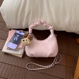 Sac nuage plissé rose avec bandoulière tressée et charm ours en peluche sur parquet