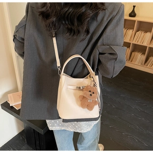 Close-up of cream bucket bag featuring metal lock and cute brown bear charm accessory