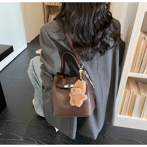 Detail of dark brown leather bucket bag with silver clasp and teddy bear charm accessory
