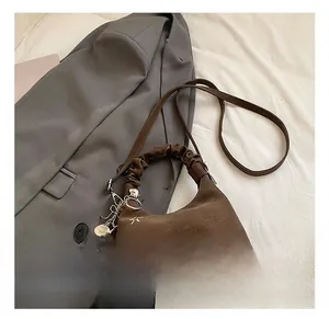 Detail of brown pleated hobo bag with star embroidery and heart charm on grey fabric