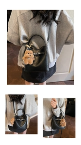 Detail view of black lychee grain leather bucket bag with silver lock and plush bear charm
