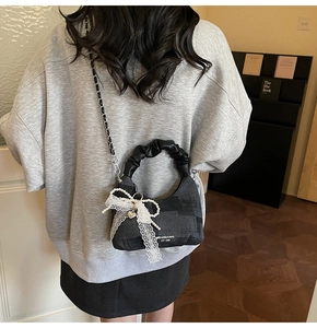 Detail of black dumpling bag featuring lace bow, pearl heart charm and ruffled handle