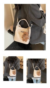 Detail of cream bucket bag with metal lock, plush bear charm and striped scarf