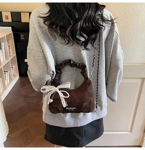 Detail of dark brown suede crescent bag with lace bow, pearl charm, and woven chain