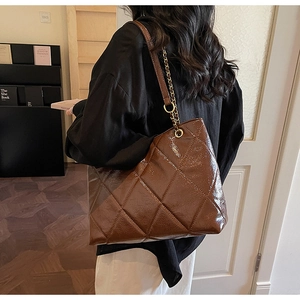 Detail of a dark brown quilted tote bag with gold chain strap on a model shoulder