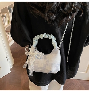 Detail of blue checkered handbag featuring a ruffle handle and pearl lace bow accessory