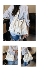 Detail view of white drawstring bucket bag with silver studs and zipper accents