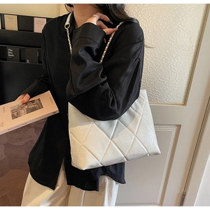 Detail of white quilted tote bag featuring a leather-woven gold chain strap on shoulder