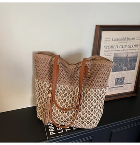 Close-up of dual-tone straw woven tote bag with leather straps and decorative tassel