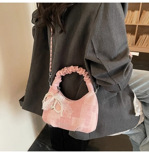 Detail of pink checkered fabric handbag with ruffled handle and white lace bow pendant