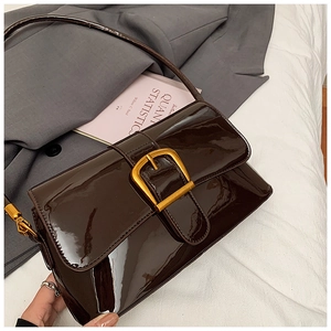Détail du sac à bandoulière en cuir verni marron foncé avec boucle dorée sur blazer gris