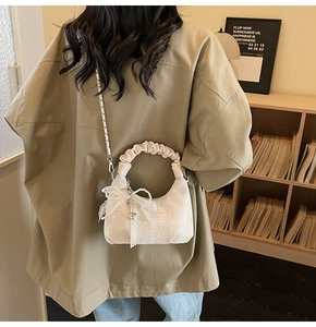 Chic beige bow handbag with pleated handle and pearl charm worn as a crossbody bag