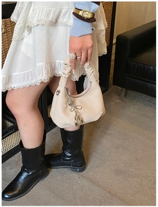 Detail of cream hobo bag featuring floral embroidery and a silver bow charm