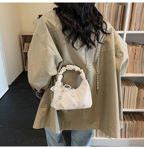Detail of a beige pleated handbag with pearl lace bow and heart charm on a metal chain