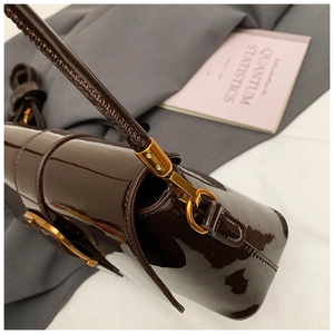 Dettaglio borsa sottobraccio in vernice marrone scuro con inserti in metallo dorato