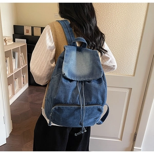 Détail d'un sac à dos en jean bleu montrant le cordon de serrage et le rabat sur modèle