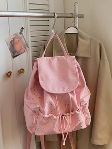 Pink casual backpack with silver star patterns hanging on a metal rack in a cozy room