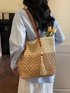 Two-tone woven straw tote bag with leather straps and decorative tassel on a blue shirt