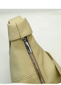 Macro view of silver zipper detail and beige lychee pattern leather on the handbag