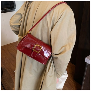 Dettaglio borsa a tracolla in vernice rossa con fibbia dorata indossata su un cappotto beige