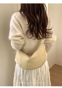 Close-up of minimalist beige crescent leather bag worn by model with retro vibe
