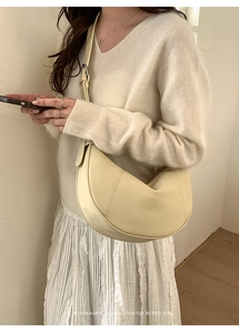 Detail of minimalist beige half-moon shoulder bag showing textured faux leather and stitching
