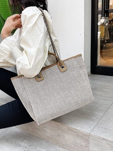 Bolso tote grande de lona beige con ribete de cuero marrón y cadena mostrado por modelo
