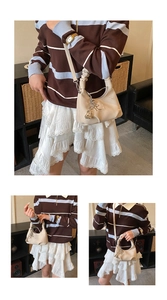 Detail of cream crossbody dumpling bag featuring floral embroidery and ribbon pendant charm